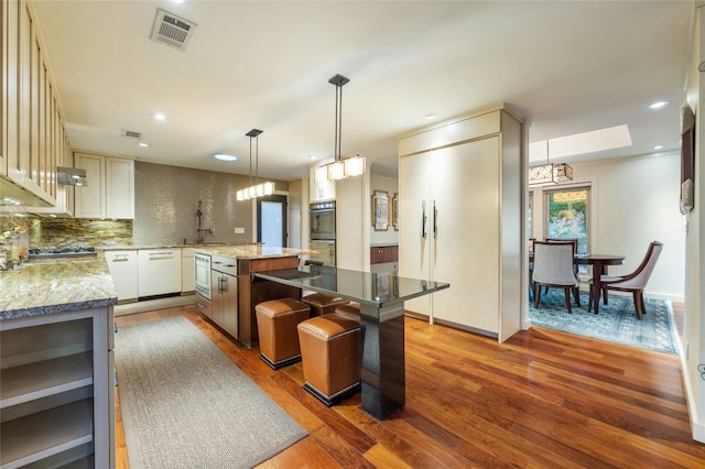 kitchen featuring a kitchen island, dark hardwood / wood-style floors, hanging light fixtures, backsplash, and light stone counters