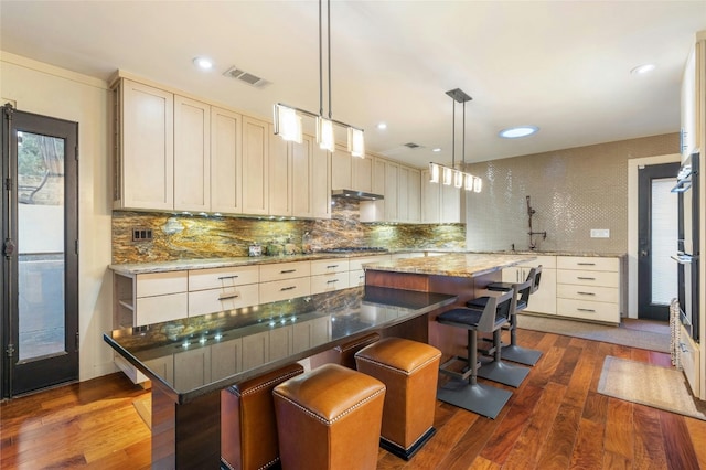 kitchen with backsplash, dark hardwood / wood-style floors, a kitchen bar, and a kitchen island