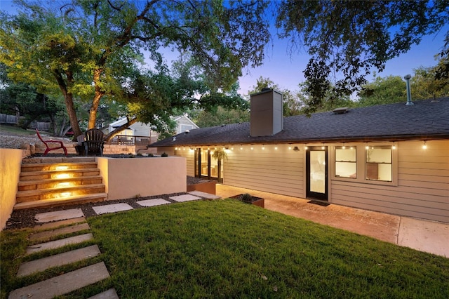 back house at dusk with a patio area and a lawn