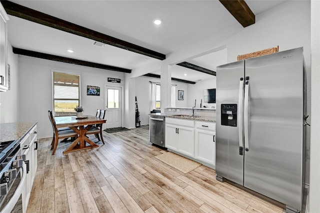 kitchen with appliances with stainless steel finishes, light stone countertops, white cabinetry, light hardwood / wood-style floors, and beamed ceiling