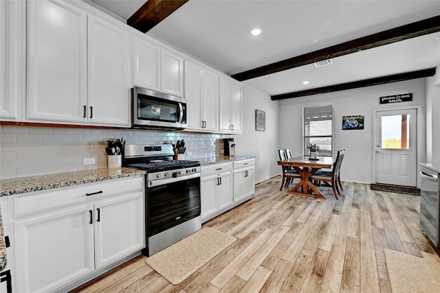 kitchen featuring appliances with stainless steel finishes, white cabinets, and beamed ceiling