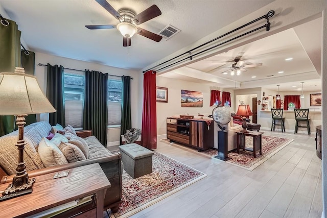 living room featuring ceiling fan, light hardwood / wood-style floors, and a raised ceiling