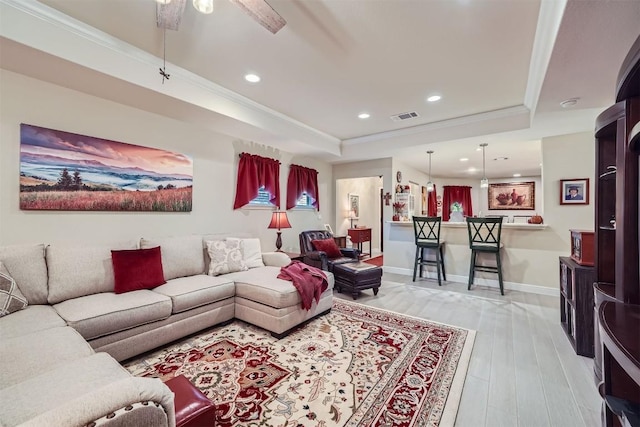 living room with a raised ceiling, crown molding, and light wood-type flooring