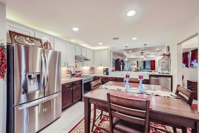 kitchen featuring kitchen peninsula, backsplash, stainless steel appliances, white cabinets, and light hardwood / wood-style floors