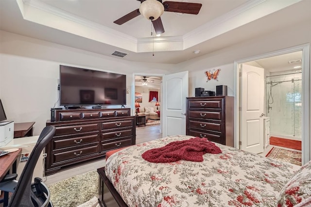 bedroom featuring ceiling fan, ornamental molding, connected bathroom, a tray ceiling, and light hardwood / wood-style floors