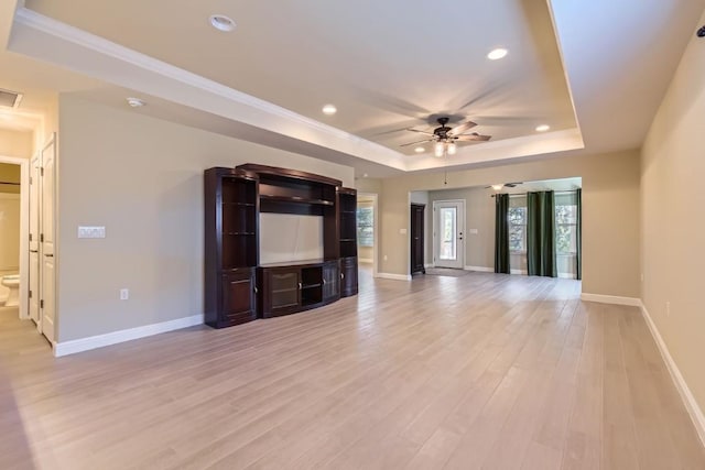 unfurnished living room featuring ceiling fan, light wood-type flooring, ornamental molding, and a tray ceiling