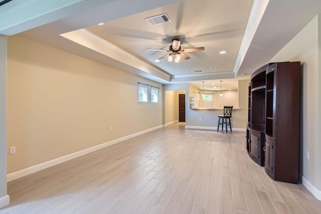 unfurnished living room featuring a tray ceiling, ceiling fan, crown molding, and light wood-type flooring