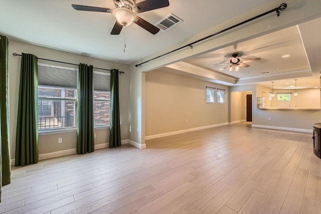 unfurnished room with a raised ceiling, a wealth of natural light, and light hardwood / wood-style flooring