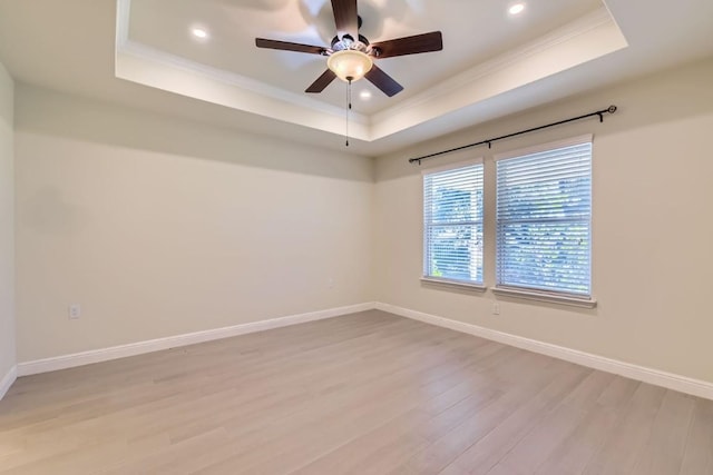 spare room with ceiling fan, a raised ceiling, light wood-type flooring, and crown molding