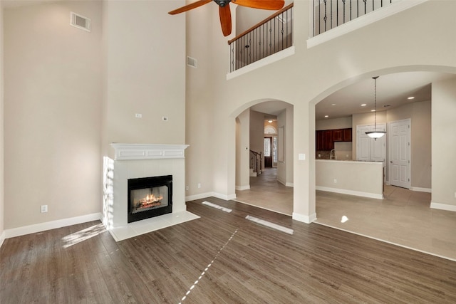 unfurnished living room with a towering ceiling, sink, a fireplace, dark hardwood / wood-style flooring, and ceiling fan