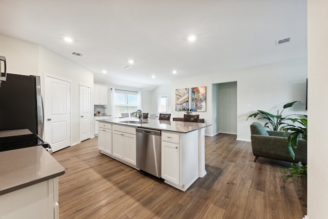 kitchen with white cabinetry, appliances with stainless steel finishes, hardwood / wood-style floors, and a kitchen island with sink