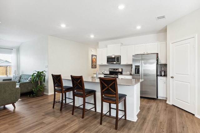 kitchen featuring a breakfast bar area, appliances with stainless steel finishes, an island with sink, white cabinetry, and dark wood-type flooring