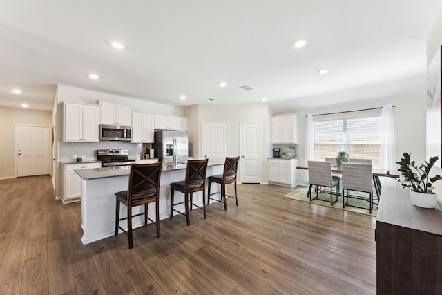 kitchen featuring dark hardwood / wood-style floors, appliances with stainless steel finishes, a center island with sink, and white cabinets