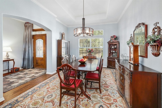 dining room featuring a notable chandelier, ornamental molding, light wood-type flooring, and a raised ceiling