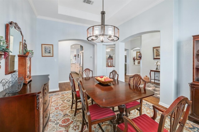 dining space with an inviting chandelier, ornamental molding, a tray ceiling, and light wood-type flooring