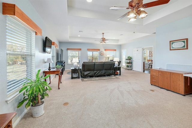 living room with light carpet, a tray ceiling, and ceiling fan