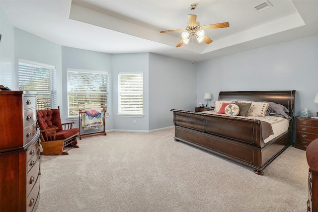 bedroom with ceiling fan, a tray ceiling, multiple windows, and light colored carpet