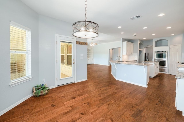 1900 County Road 245, Georgetown, TX 78633 - kitchen featuring double oven, arched walkways, white cabinetry, a peninsula, and dark wood-style flooring