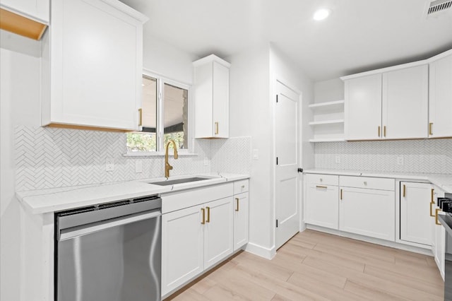 kitchen with light stone countertops, white cabinetry, sink, stainless steel dishwasher, and light wood-type flooring