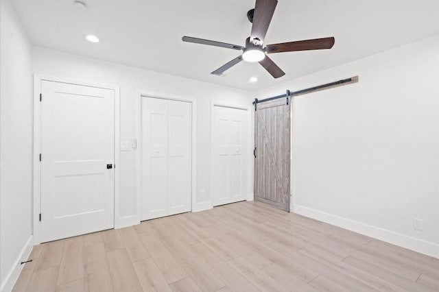 unfurnished bedroom with a barn door, ceiling fan, light hardwood / wood-style floors, and two closets