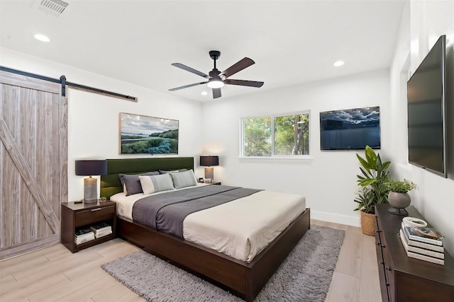 bedroom featuring a barn door, ceiling fan, and light hardwood / wood-style flooring