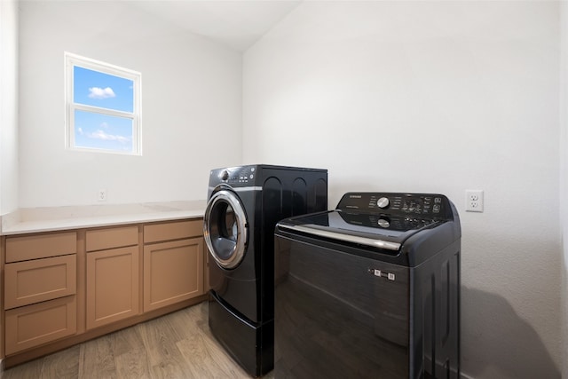 clothes washing area with separate washer and dryer, light wood-type flooring, and cabinets