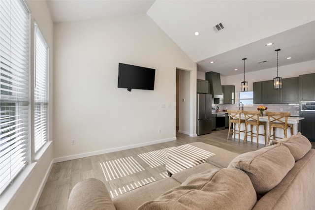 living room with high vaulted ceiling, a healthy amount of sunlight, and light hardwood / wood-style flooring