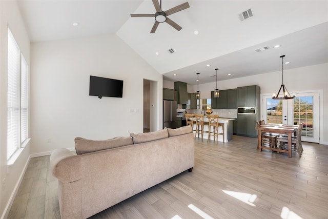 living room with high vaulted ceiling, light hardwood / wood-style flooring, and ceiling fan with notable chandelier