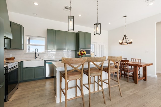 kitchen with a kitchen island, light hardwood / wood-style flooring, hanging light fixtures, sink, and appliances with stainless steel finishes