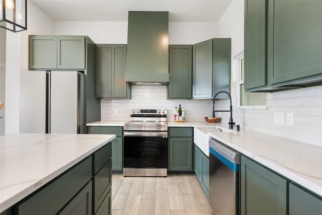 kitchen featuring light stone countertops, wall chimney range hood, green cabinetry, stainless steel appliances, and pendant lighting