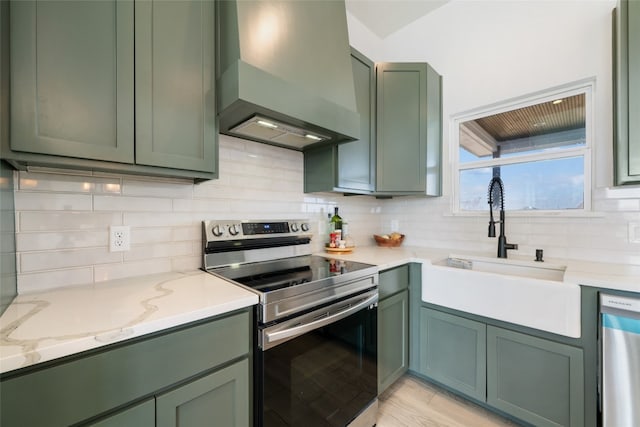 kitchen with appliances with stainless steel finishes, decorative backsplash, green cabinetry, and wall chimney range hood