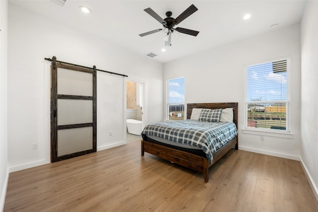 bedroom featuring ensuite bath, light hardwood / wood-style flooring, a barn door, and ceiling fan