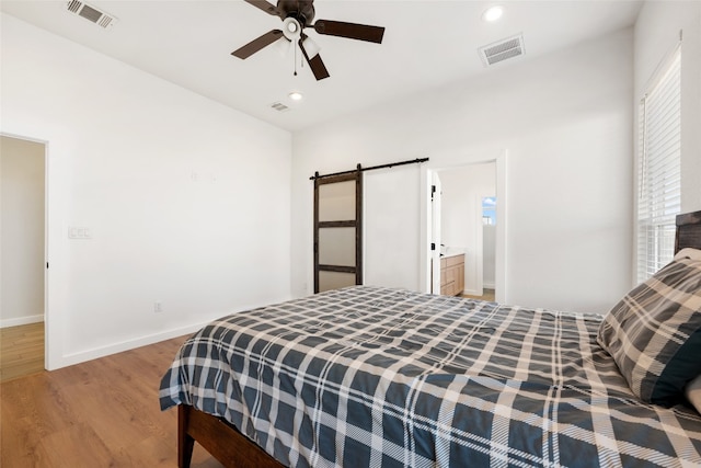 bedroom with light hardwood / wood-style flooring, a barn door, ensuite bathroom, and ceiling fan