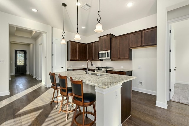 kitchen with light stone counters, dark hardwood / wood-style flooring, appliances with stainless steel finishes, sink, and decorative light fixtures