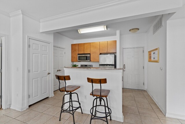 kitchen featuring ornamental molding, a kitchen breakfast bar, appliances with stainless steel finishes, and light tile patterned flooring