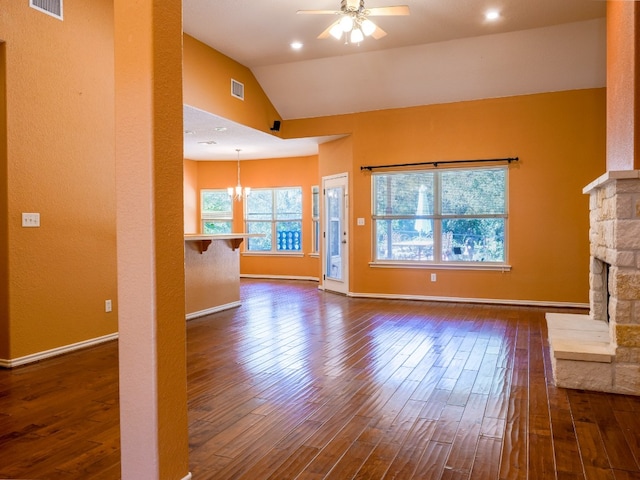 unfurnished living room featuring a stone fireplace, ceiling fan with notable chandelier, vaulted ceiling, and dark hardwood / wood-style flooring