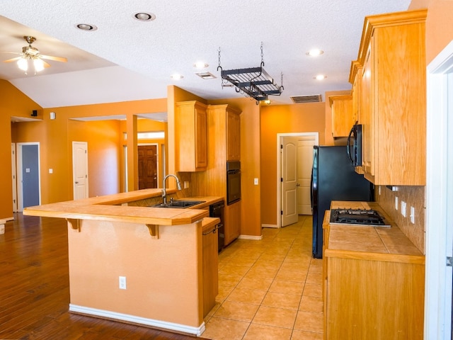 kitchen with a breakfast bar area, sink, tile counters, and black appliances