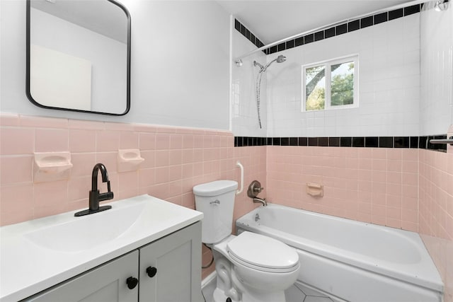 full bathroom with toilet, tiled shower / bath combo, vanity, and tile walls