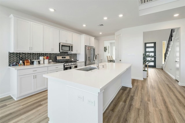 kitchen featuring sink, a kitchen island with sink, stainless steel appliances, and white cabinetry