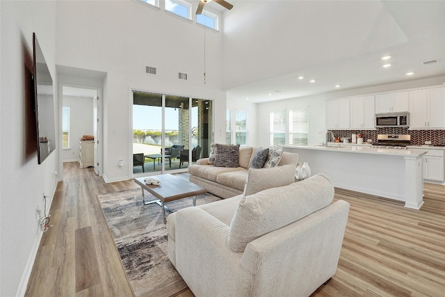 living room with ceiling fan, a towering ceiling, sink, and light wood-type flooring