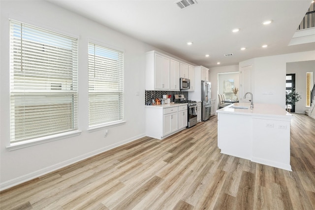 kitchen with white cabinets, a center island with sink, sink, light hardwood / wood-style floors, and stainless steel appliances