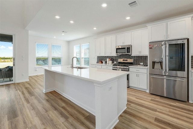 kitchen with white cabinets, a center island with sink, light hardwood / wood-style flooring, sink, and stainless steel appliances