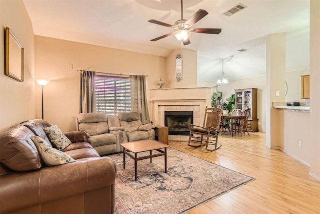 living room with ceiling fan, light wood-type flooring, a tile fireplace, and lofted ceiling