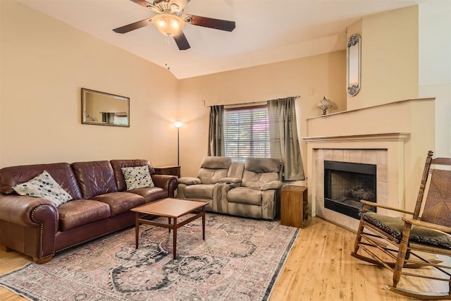 living room with ceiling fan, light wood-type flooring, a tile fireplace, and vaulted ceiling