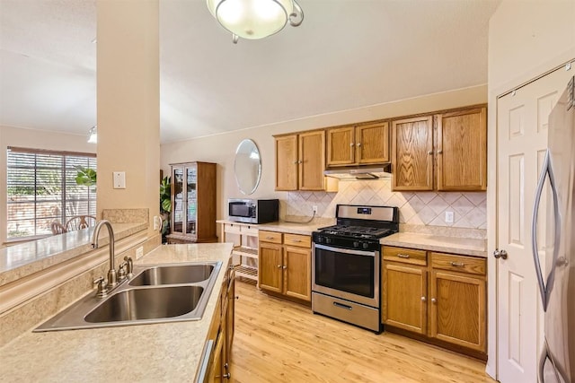 kitchen with decorative backsplash, light wood-type flooring, stainless steel appliances, vaulted ceiling, and sink