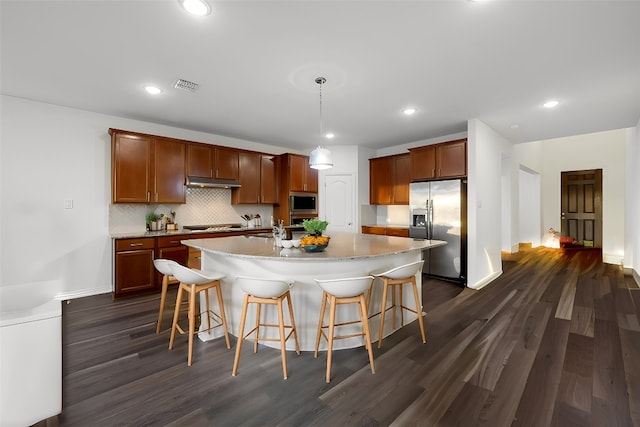 kitchen with a kitchen island with sink, a breakfast bar area, decorative light fixtures, appliances with stainless steel finishes, and dark hardwood / wood-style flooring