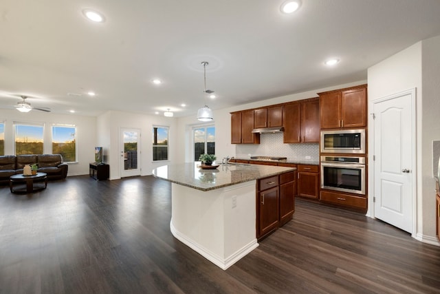 kitchen with appliances with stainless steel finishes, dark wood-type flooring, pendant lighting, and a kitchen island