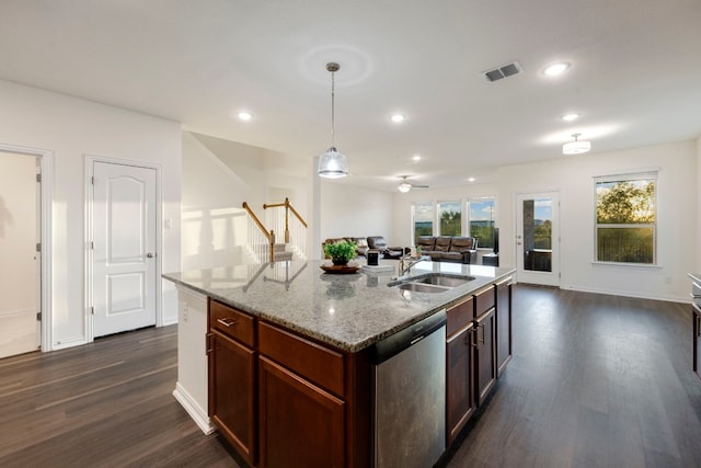 kitchen with a center island with sink, hanging light fixtures, light stone countertops, dishwasher, and dark wood-type flooring