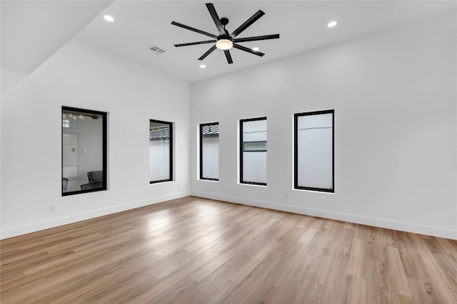 unfurnished room featuring light hardwood / wood-style flooring, a towering ceiling, and ceiling fan