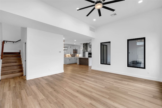 unfurnished living room featuring ceiling fan, a towering ceiling, sink, and light wood-type flooring